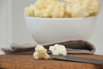 A cauliflower piece split in half on a wooden surface with a white bowl and napkin in the background.