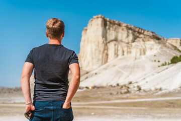 Rear view of a young man standing and looking out over a huge white rock, concept of travel and freedom, Crimea 