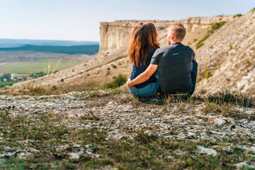 Rear view of couple in love a man and a woman sit on the edge of a cliff overlooking the White rock and the surrounding area in Crimea