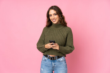 Young woman over isolated pink background sending a message with the mobile