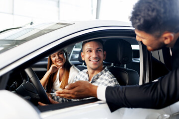 Young couple choosing a car at the dealership with manager helping