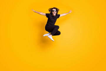 Full length body size portrait of man jumping high wearing black casual outfit sunglass shouting isolated on bright yellow color background