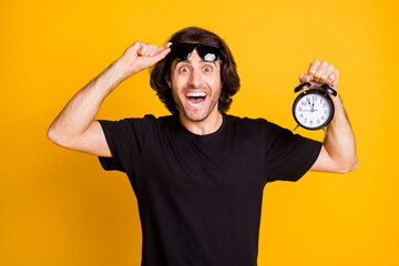 Photo of young man hold alarm clock show dial take off glasses wear t-shirt sunglass isolated...