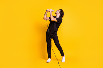 Fototapeta na wymiar Full length profile photo of young man hold mic sing open mouth wear black t-shirt pants white sneakers glasses isolated yellow color background