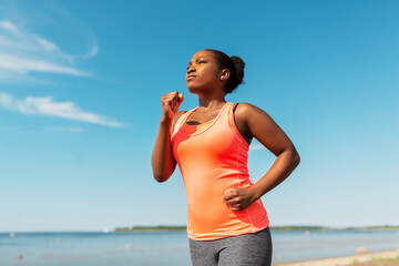 fitness, sport and healthy lifestyle concept - young african american woman running at seaside