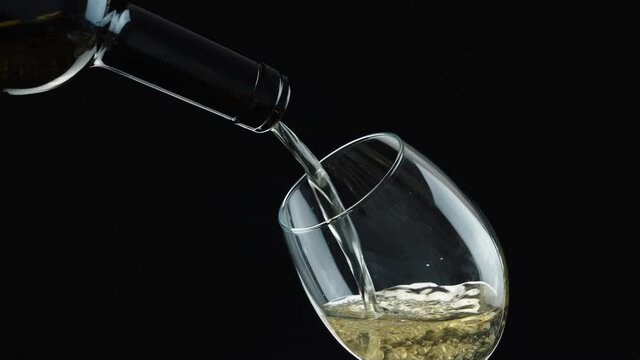 White wine. Pouring white wine from the bottle into a wineglass. Wine in glass on black background.