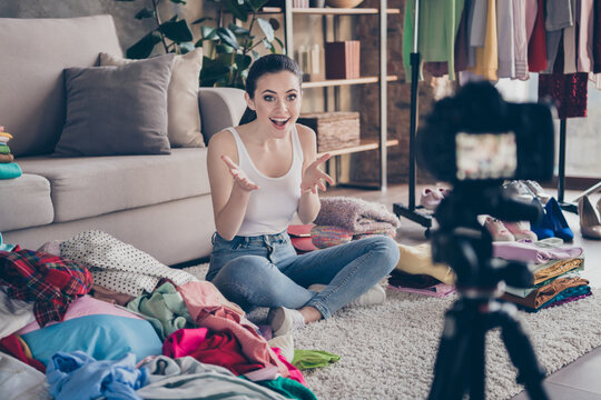 Full body photo of astonished positive girl blogger sit floor carpet legs crossed filming camera tell incredible black friday bargain surround fabric pile dressing in house indoors
