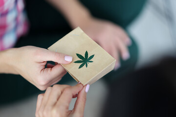 Female hand holds paper bag with an image of marijuana symbol closeup. Online delivery of marijuana...