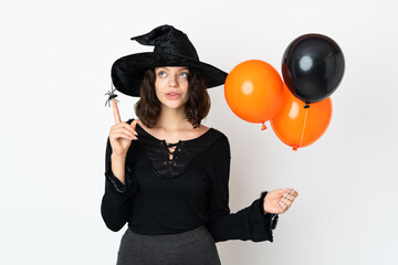 Young witch holding black and orange air balloons thinking an idea pointing the finger up