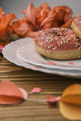 Pink donuts decorated with colorful sprinkles on a white plate on a wooden table. Close up