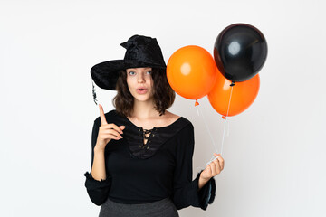 Young witch holding black and orange air balloons intending to realizes the solution while lifting a finger up