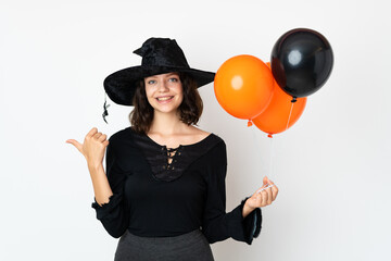 Young witch holding black and orange air balloons pointing to the side to present a product