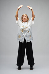 Mature blonde woman practicing Chi kung and Tai Chi on a white background. She wears a traditional white chinese Tai Chi jacket, black trousers and black shoes with ying yang symbol