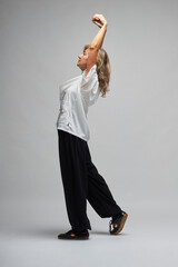 Mature blonde woman practicing Chi kung and Tai Chi on a white background. She wears a traditional white chinese Tai Chi jacket, black trousers and black shoes with ying yang symbol