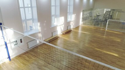 Empty school gym. A volleyball net is stretched in the center of the hall. Sports equipment and a tennis table are located against the wall
- Powered by Adobe