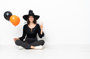 Young witch holding black and orange air balloons sitting on the floor pointing up a great idea