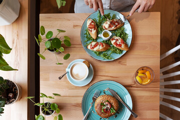 Colorful table full of healthy food for lunch in restaurant. Vegan burger, breadstuff with vegetables and hands of woman eat lunch. Top view.