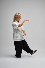 Mature blonde woman practicing Chi kung and Tai Chi on a white background. She wears a traditional white chinese Tai Chi jacket, black trousers and black shoes with ying yang symbol