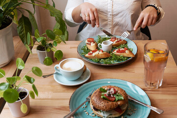 Vegetarian food on a plate with coffee on lunch in restaurant. Hands of woman with cutlery eat a healthy meal for breakfast. Close up.