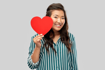 love, charity and valentines day concept - happy asian young woman with red heart over grey background