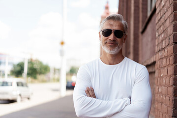 Portrait of a Grey-haired Mature handsome man in jeans and white t-shirt leaning to the old wall.