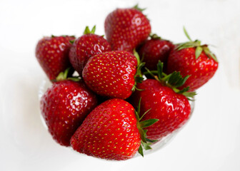large red strawberries in a glass plate on a white background top view. red fruit is close
