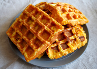 four fresh Belgian waffles made from cornmeal, eggs and pumpkin lie on a grey round plate on a beige tablecloth side view . gluten-free homemade food
