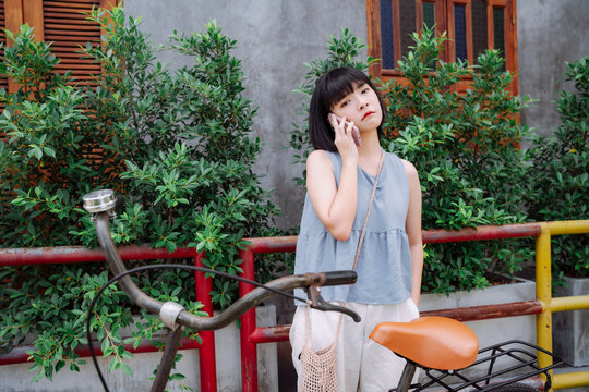 Young asian woman travel calling mechanic with smartphone to fix the broken bicycle.