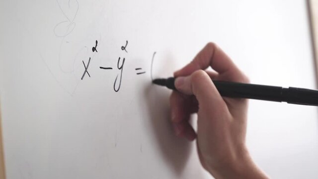 Female hand writes a formula with a marker on a white board