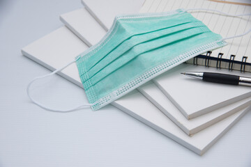 Medical mask, notebook with pen and book on white