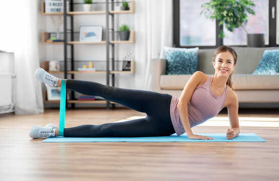 sport, fitness and people concept - happy woman exercising with resistance band lying on mat at home