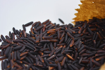 Delicious healthy black wild long rice sprinkled from brown paper bag on white backdrop. Healthy food, healthy cereals for human life.