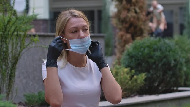 Portrait of pretty young woman in black gloves looking into the camera and putting on medical mask on face for protection against coronavirus nCov-19. COVID-19 preventive measures. Slow motion. Close