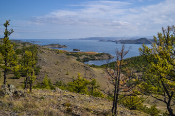 Autumn view of bay of Lake Baikal with islands and peninsulas and mountains on horizon. Blue water, yellow and green trees. Siberia landscape