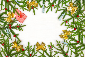 Frame of decorated natural green Christmas tree branches with red gift box on white wooden background. Empty space for text