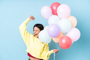 Fototapeta na wymiar Woman holding balloons in a party over isolated blue background celebrating a victory