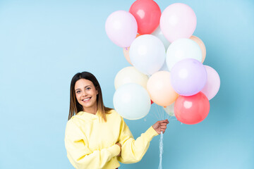 Fototapeta na wymiar Woman holding balloons in a party over isolated blue background looking to the side