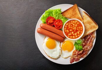 plate of fried eggs with bacon, beans, sausages, toasts and tomatoes, top view