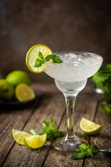 Cocktail margarita garnished with lime and mint on wooden background