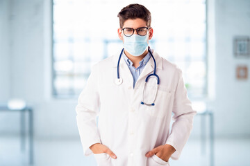 Portrait of male doctor wearing face mask while standing in the hospital foyer