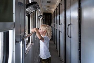 Fototapeta na wymiar Blond boy looks curiously at the train window. Traveling with children