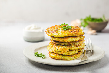 Green zucchini fritters, vegetarian zucchini pancakes with fresh herbs and garlic, served with cream sauce on white background, selective focus