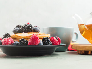 Stack of pancakes with fresh berries served in a dish with green tea. Hero view