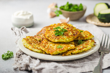 Green zucchini fritters, vegetarian zucchini pancakes with fresh herbs and garlic, served with cream sauce on white background, selective focus