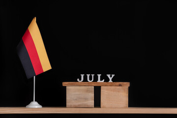 Wooden calendar of July with table German flag on black background. Holidays of German in July.