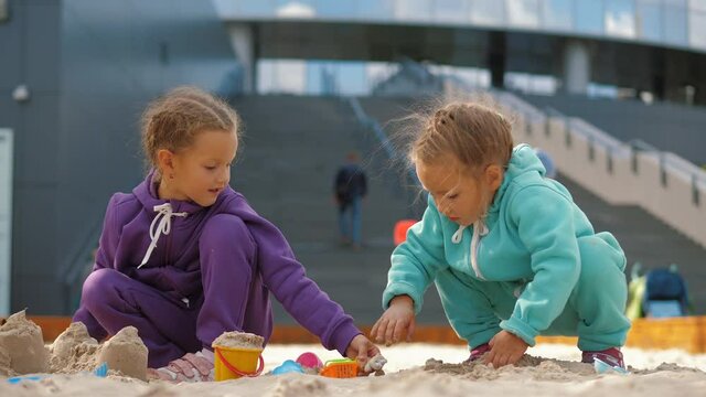 Two children 4-5 years old sitting in sandbox, playing with toys and buckets