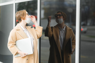 Young attractive girl in medical mask on face with laptop walking  in the city