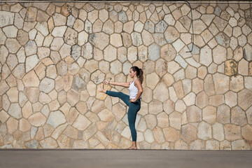 Strong Yoga teacher woman doing an intensive workout along the beach against a seamless pattern wall. Young and attractive woman doing Yoga and Pilates exercises outdoor during a fresh summer day