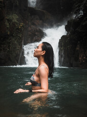side view of sexy asian woman in bikini standing in tropical waterfall. 