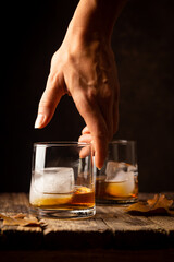 Glass of scotch whiskey and ice on wooden background with hand